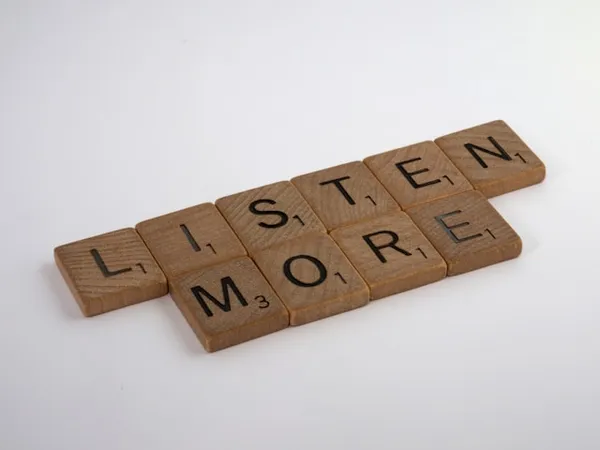 Houten Scrabble-tegels gerangschikt tot de woorden LISTEN en MORE.