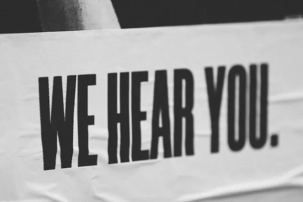 Zwart-witte banner met grote, dikke letters: WE HEAR YOU.