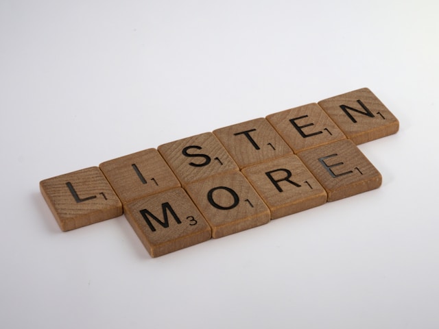 Houten Scrabble-tegels gerangschikt tot de woorden LISTEN en MORE.