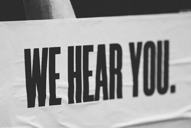 Zwart-witte banner met grote, dikke letters: WE HEAR YOU.